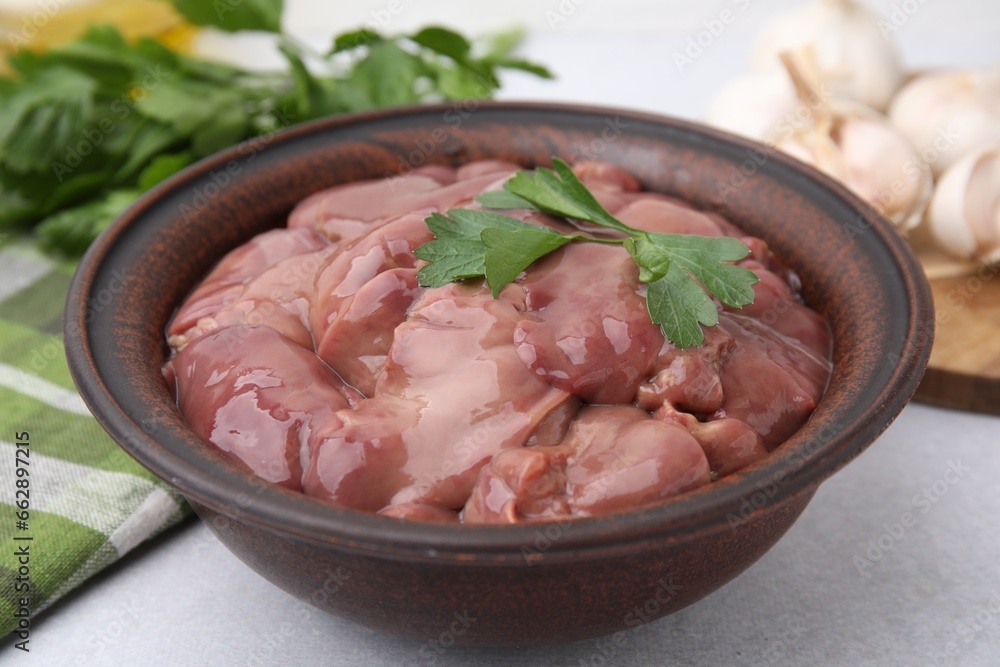 Bowl with raw chicken liver and parsley on white table