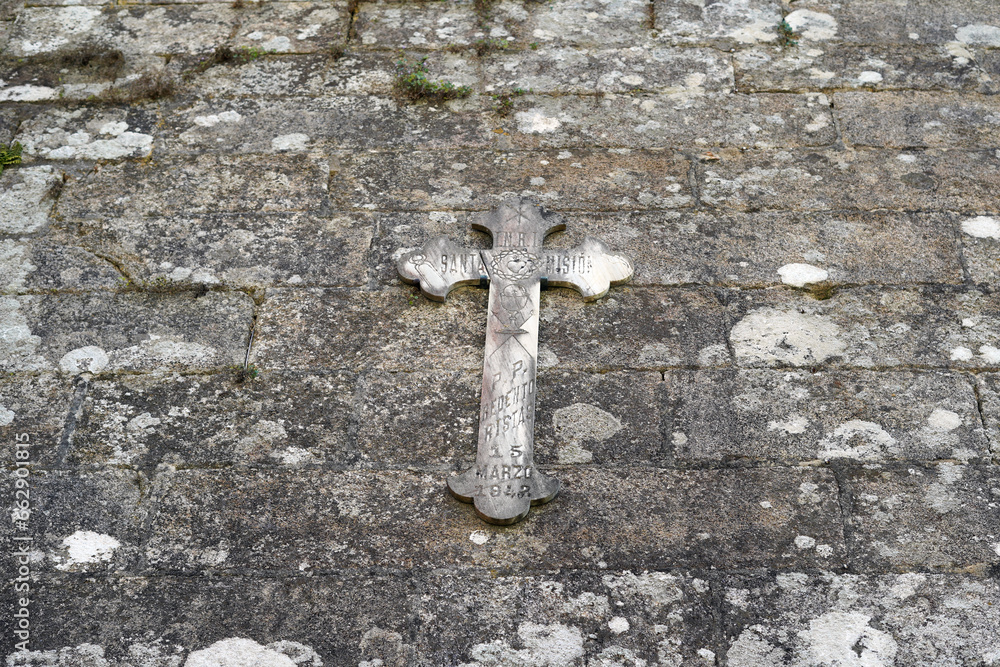 The gray stone wall of the church, on which there is a bland symbol of the cross.