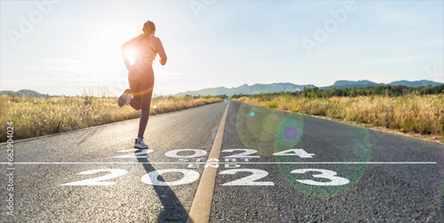 New year 2024 or start straight concept.word 2024 written on the asphalt road and athlete woman runner stretching leg preparing for new year at sunset.Concept of challenge or career path and change. photo