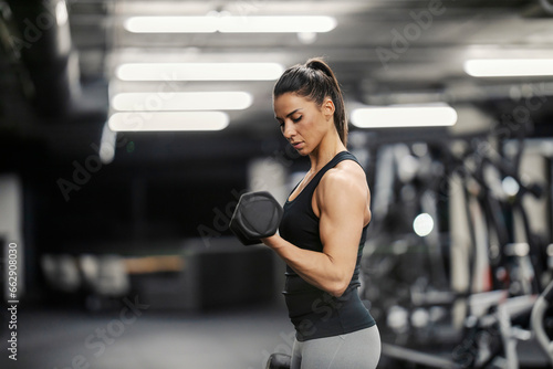 Side view of a strong woman with big muscles doing workouts in a gym with dumbbells.