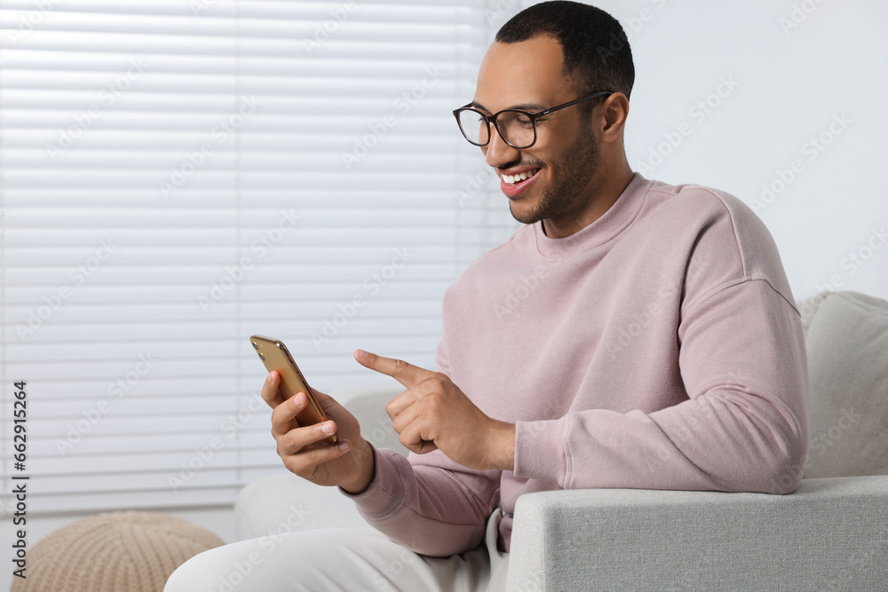 Happy man sending message via smartphone at home Happy man sending message via smartphone at home