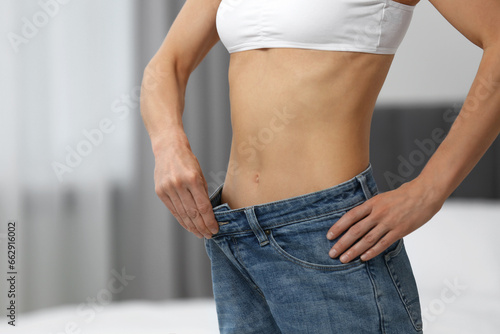 Slim woman wearing big jeans at home, closeup. Weight loss