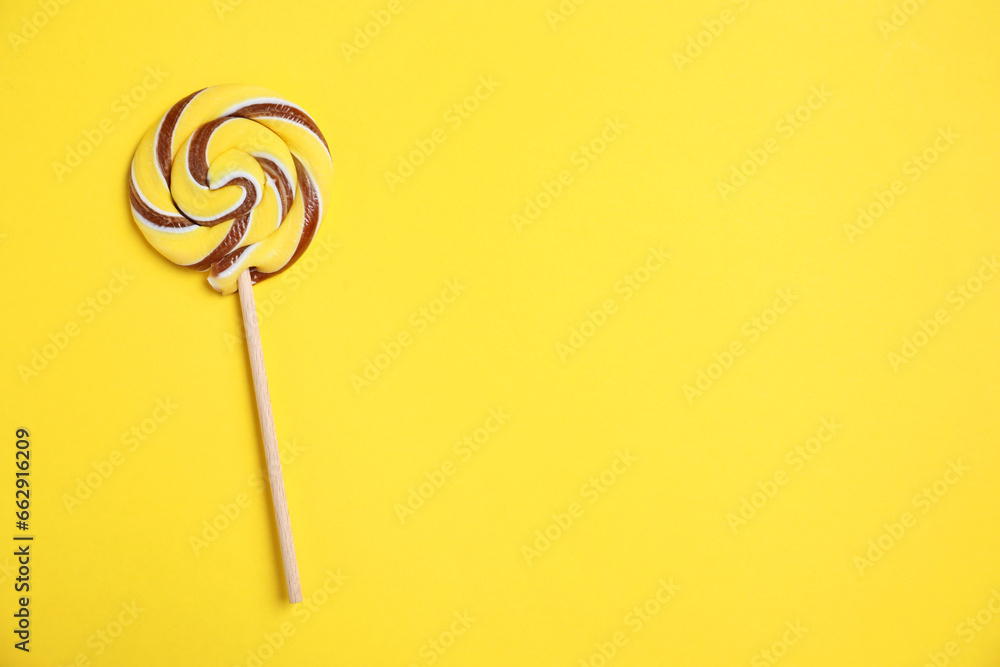 Stick with colorful lollipop swirl on yellow background, top view. Space for text Stick with colorful lollipop swirl on yellow background, top view. Space for text