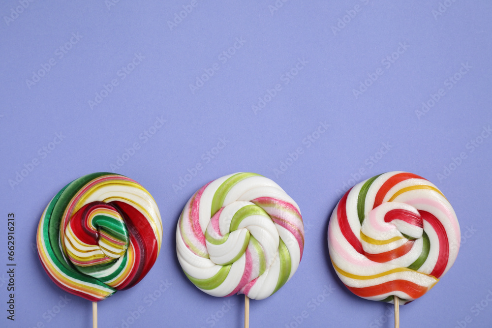 Sticks with different colorful lollipops on violet background, flat lay. Space for text Sticks with different colorful lollipops on violet background, flat lay. Space for text