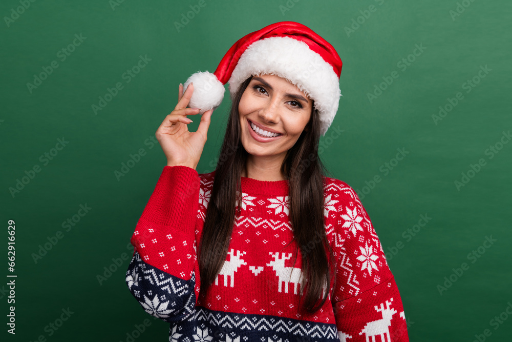 Photo of cute positive person beaming smile arm hold newyear headwear pompom isolated on green color background Photo of cute positive person beaming smile arm hold newyear headwear pompom isolated on green color background