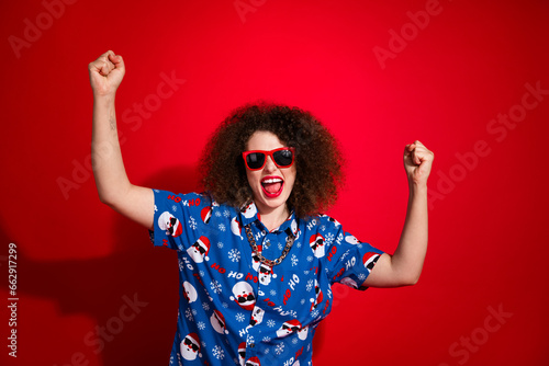 Photo of lucky excited woman wear ugly santa claus print x-mas shirt screaming yes isolated red color background