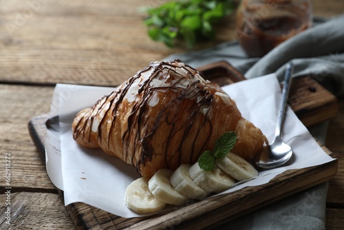 Delicious croissant with chocolate, banana and spoon on wooden table