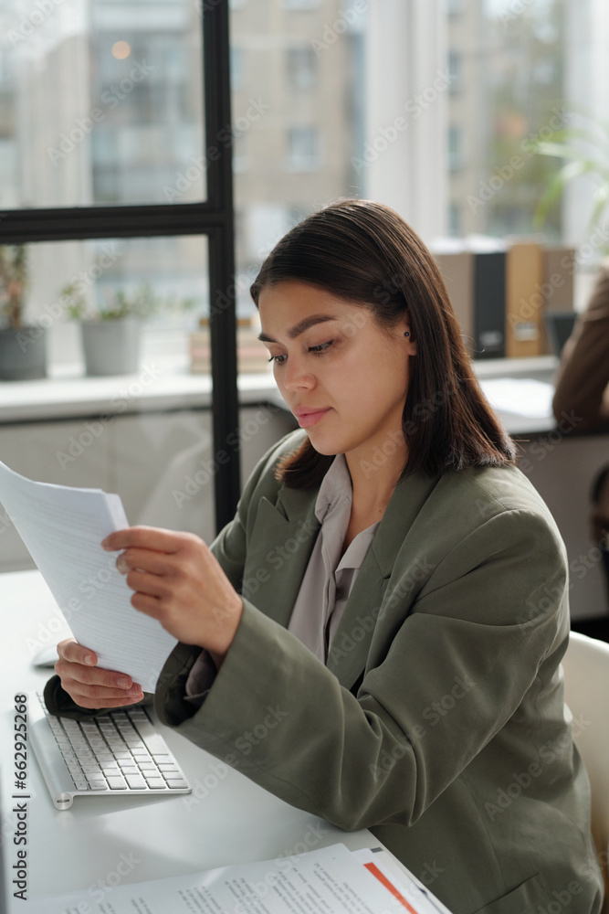 Young female secretary in formalwear looking through financial papers while preparing documents for negotiation and making business deal Young female secretary in formalwear looking through financial papers while preparing documents for negotiation and making business deal