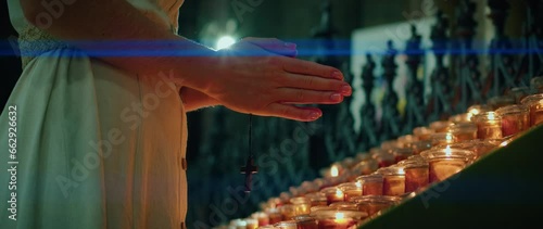 Believing girl prays near burning candles in church. Woman folded hands fervently atones for sins. photo