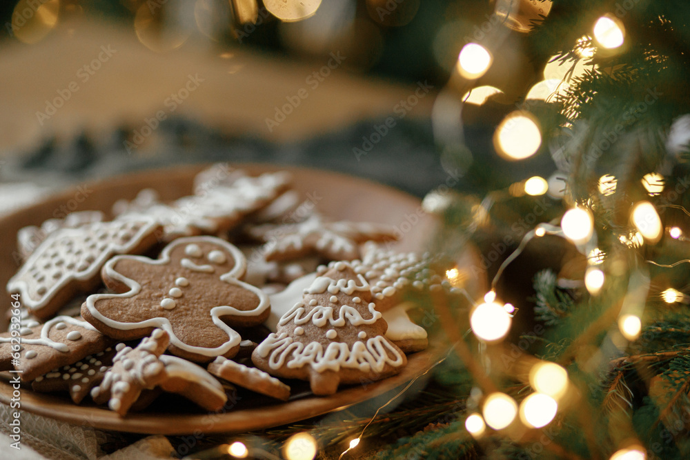 Christmas gingerbread cookies with icing in plate on festive rustic table with decorations, fir branches, golden illumination. Merry Christmas! Delicious gingerbread cookies, atmospheric time Christmas gingerbread cookies with icing in plate on festive rustic table with decorations, fir branches, golden illumination. Merry Christmas! Delicious gingerbread cookies, atmospheric time