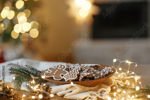 Christmas gingerbread cookies with icing in plate on festive rustic table with decorations against golden illumination. Merry Christmas! Delicious gingerbread cookies, atmospheric holiday eve