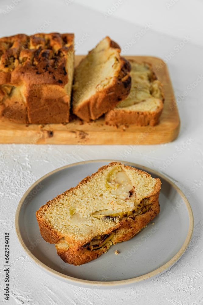 A slice of freshly baked apple fruit cake on a plate and sliced cake on a wooden cutting board