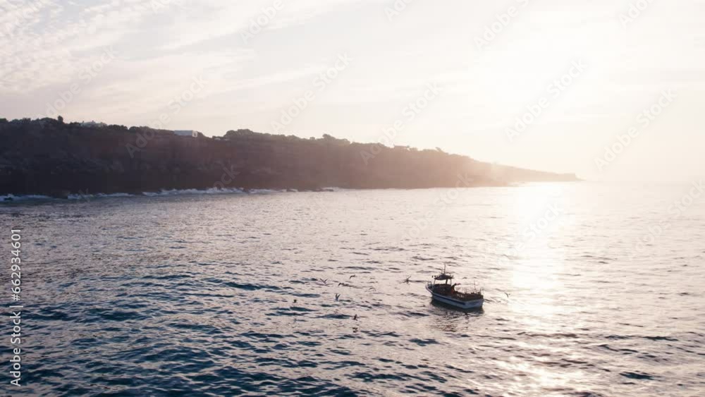 Small fishing boat off the coast of Portugal, fishing on early morning at sunrise, surrounded by seagulls. Small scale family owned fishing company Small fishing boat off the coast of Portugal, fishing on early morning at sunrise, surrounded by seagulls. Small scale family owned fishing company