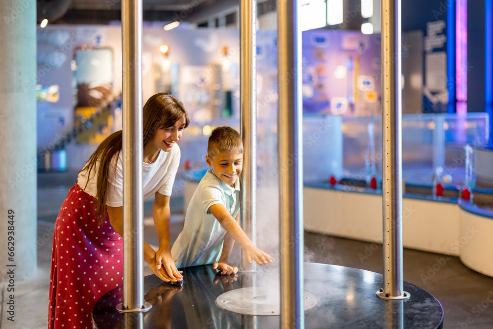 Mom with a little boy learn physics interactively on a model that shows physical phenomena while visiting a science museum. Concept of children's entertainment and learning