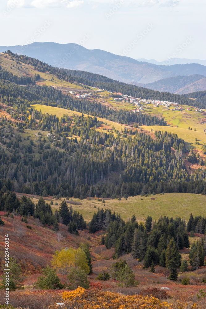 Autumn mountain landscape with colorful forest and small village in the distance.