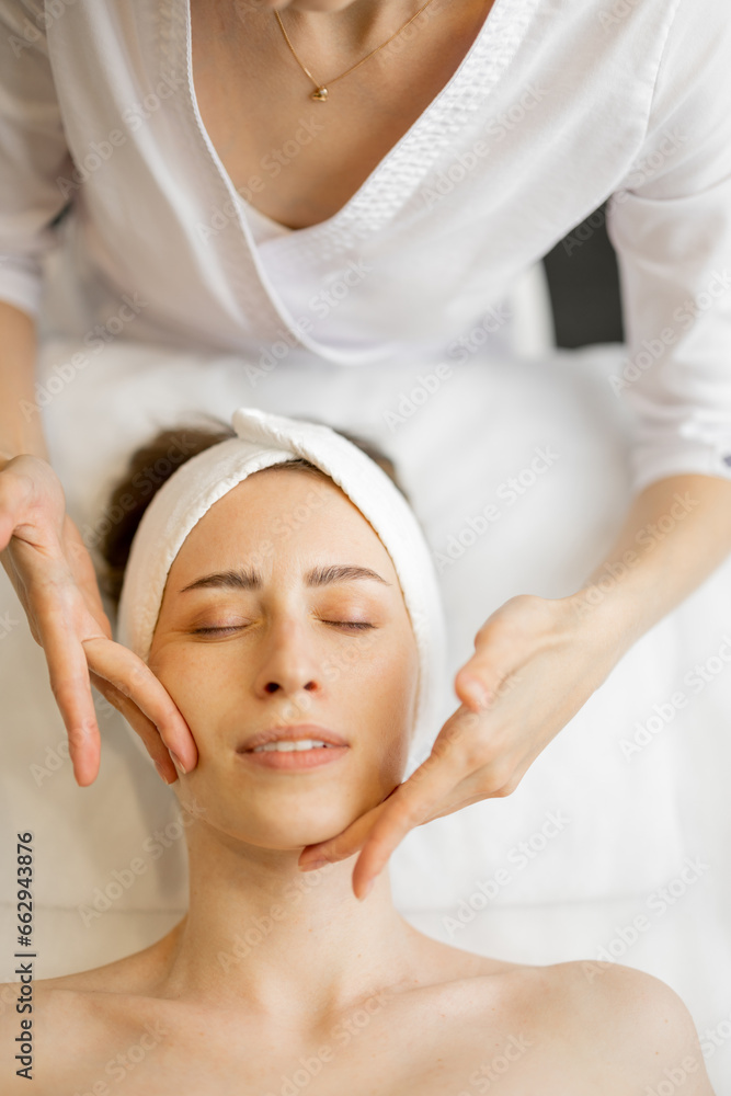 Adult woman receiving relaxing facial massage, close-up view from above on woman's face during a massage. Beautiful pose of masseur's fingers