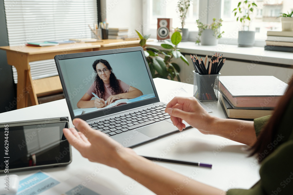 Fototapeta premium Clever multiethnic schoolgirl on laptop screen looking at teacher explaining grammar rule and listening to her during online lesson