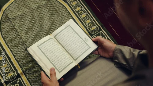 Muslim man reading The Quran holy book on a prayer mat. TRANSLATION of the muslim prayer: 