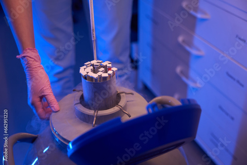 Lab scientist immersing samples into liquid nitrogen dewar for storage photo