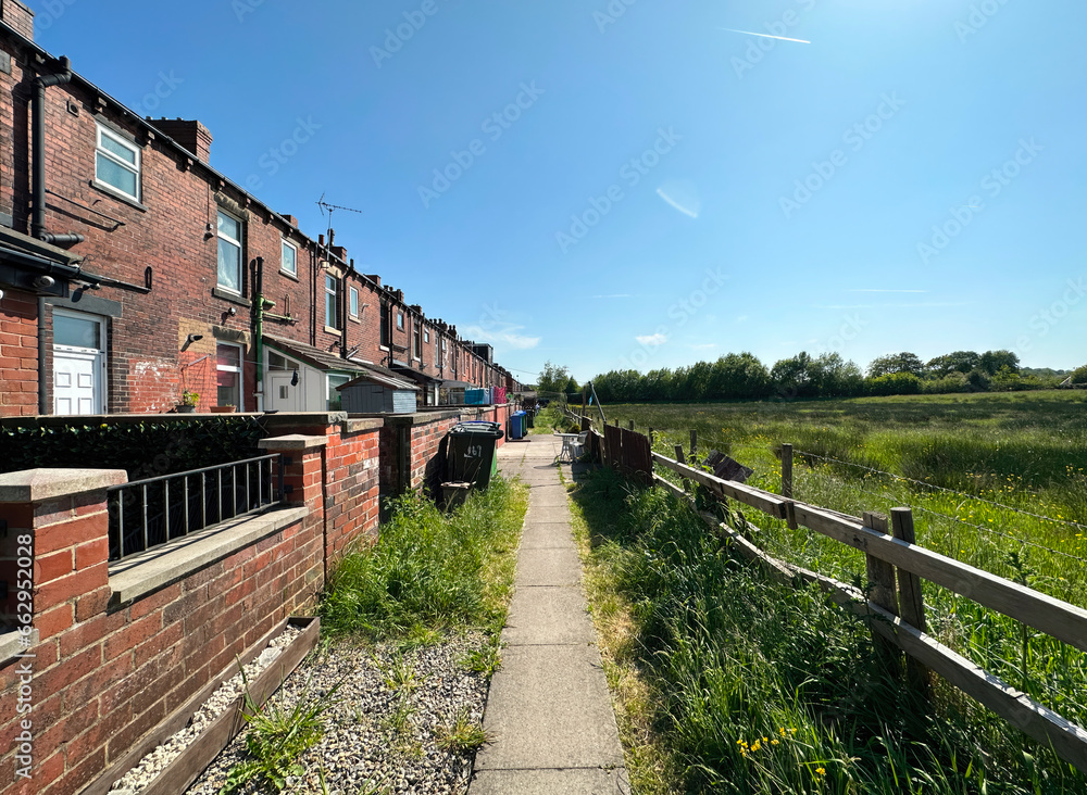 Pathway, close to a row of, old red brick terrace houses, overlooking a field, with wild plants and grasses in, Littleborough, UK