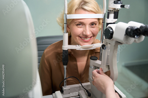 Smiling blonde sits in front of a special ophthalmic device