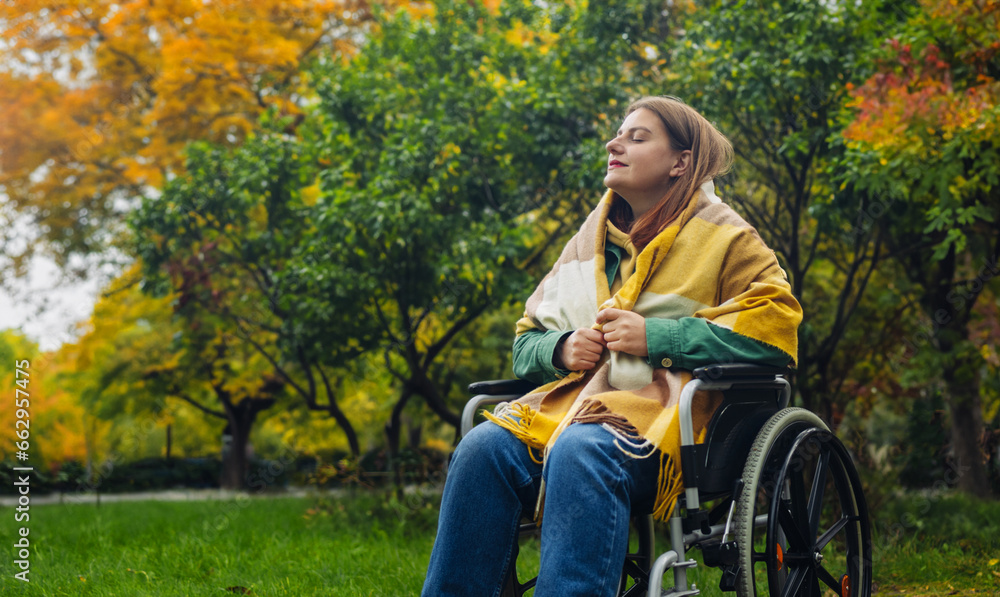 Happy smiling cheerful Caucasian woman in stylish clothes on a wheelchair relaxing alone in autumn garden park Happy smiling cheerful Caucasian woman in stylish clothes on a wheelchair relaxing alone in autumn garden park
