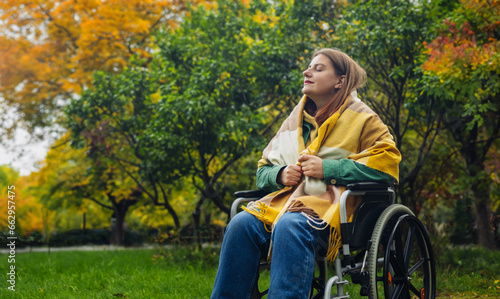Happy smiling cheerful Caucasian woman in stylish clothes on a wheelchair relaxing alone in autumn garden park © Shi 
