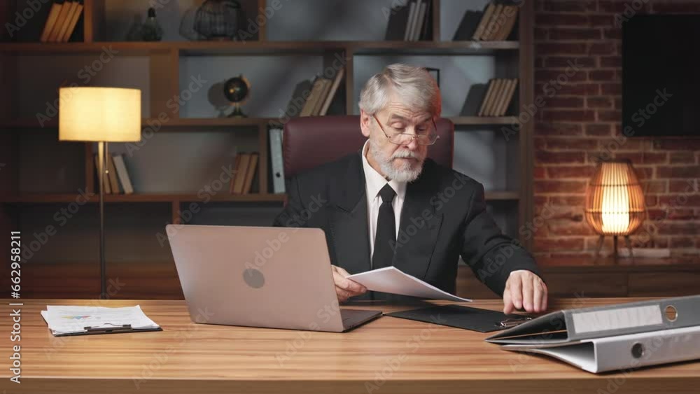 Focused aged man in glasses attaching documents on clipboard before reading information in cozy office. Well-organized employee getting files in order before fastening securely to smooth surface. Focused aged man in glasses attaching documents on clipboard before reading information in cozy office. Well-organized employee getting files in order before fastening securely to smooth surface.