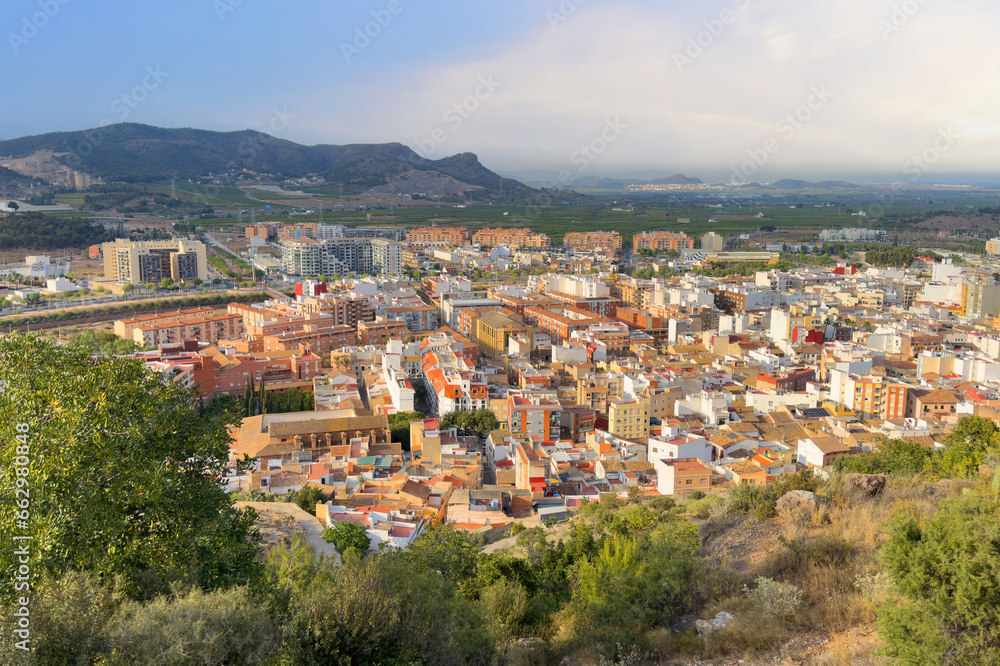 View of the city of Sagunto in Spain. Buildings, houses and streets in city. View of rooftops and streets. Town against backdrop of mountains. Roofs of houses and roofs from side of Sagunto Castle.