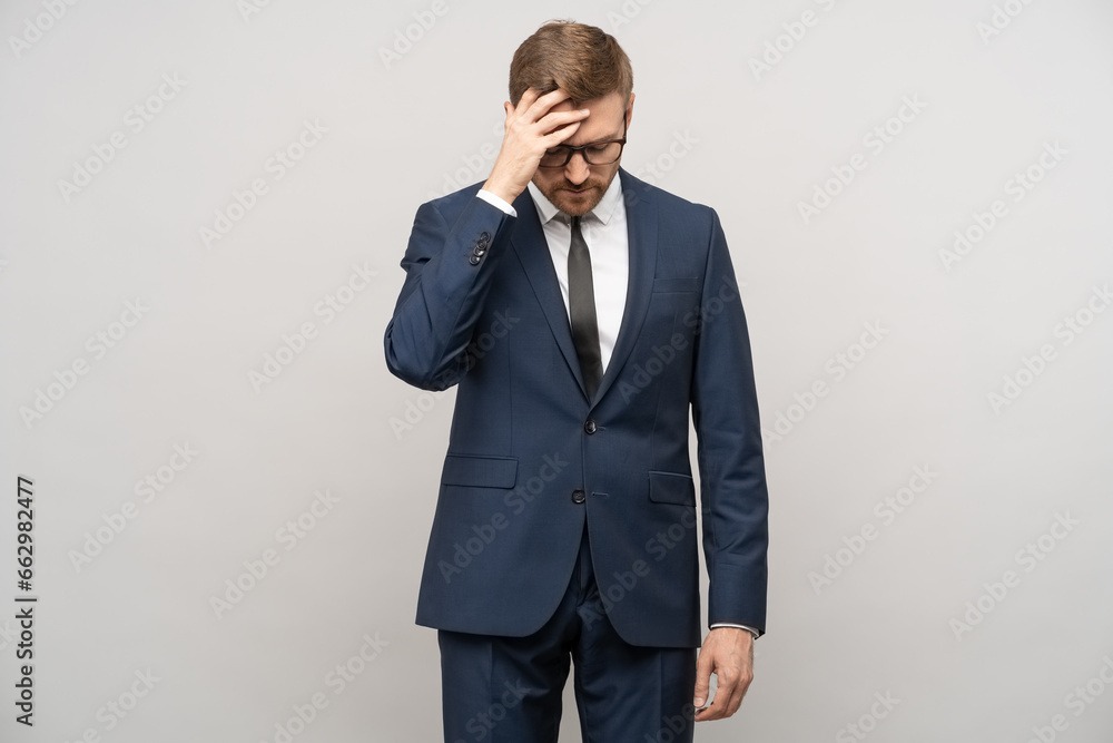 Tortured businessman trying to make decision, thinking hard about problems troubles on gray background. Man entrepreneur in suit glasses rubbing head with exhausted tired face. Headache, migraine. Tortured businessman trying to make decision, thinking hard about problems troubles on gray background. Man entrepreneur in suit glasses rubbing head with exhausted tired face. Headache, migraine.