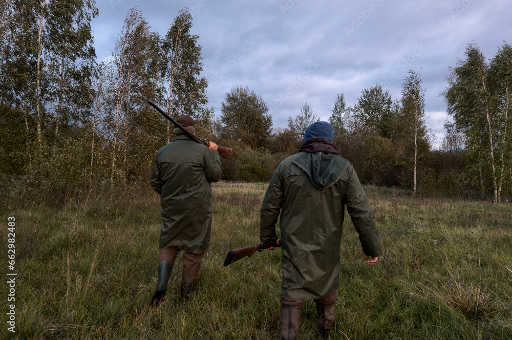 Hunters on hunt. A hunter walks through forest among trees in search of wild birds or wild animals. Hunters with gun and rifle on hunting in fall season. Hunter during hunting on elk in forest. Hunters on hunt. A hunter walks through forest among trees in search of wild birds or wild animals. Hunters with gun and rifle on hunting in fall season. Hunter during hunting on elk in forest.