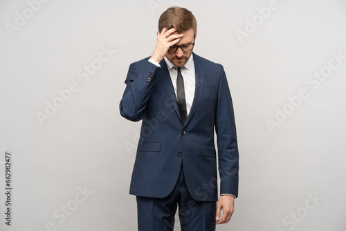 Tortured businessman trying to make decision, thinking hard about problems troubles on gray background. Man entrepreneur in suit glasses rubbing head with exhausted tired face. Headache, migraine.