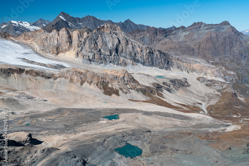 view from the top of the mountain of rocky landscape with glacier, small lakes, peaks and the valley below