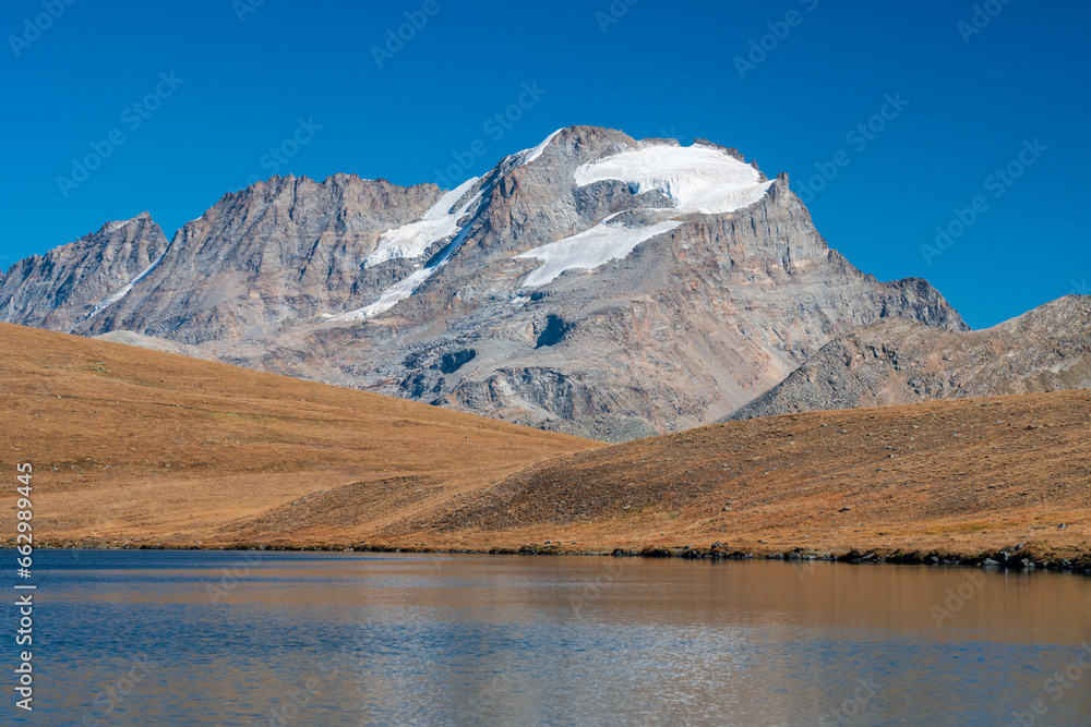 Rossett Lake with reflection, clear water foreground, meadow and gran paradiso mountain with glacier background. national park landscape in autumn. Italian Alps