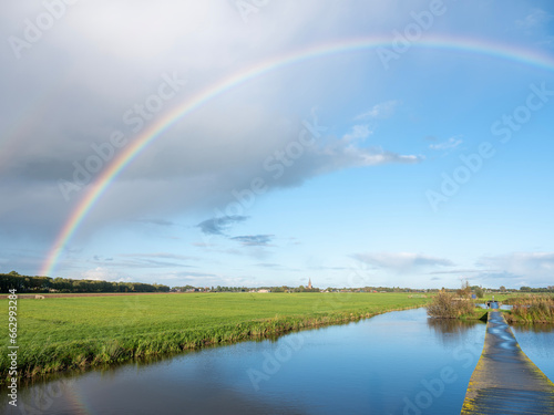 canal between dutch meadows in holland near utrecht with rainbow in blue sky