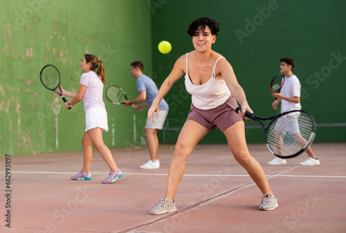 Hispanic woman pelota player hitting ball with racket during training game on outdoor Basque pelota fronton. © JackF