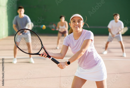 Hispanic woman pelota player hitting ball with racket during training game on outdoor Basque pelota fronton.