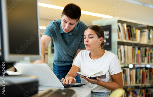 View on a young Caucasian male student teaching a female European student in the library