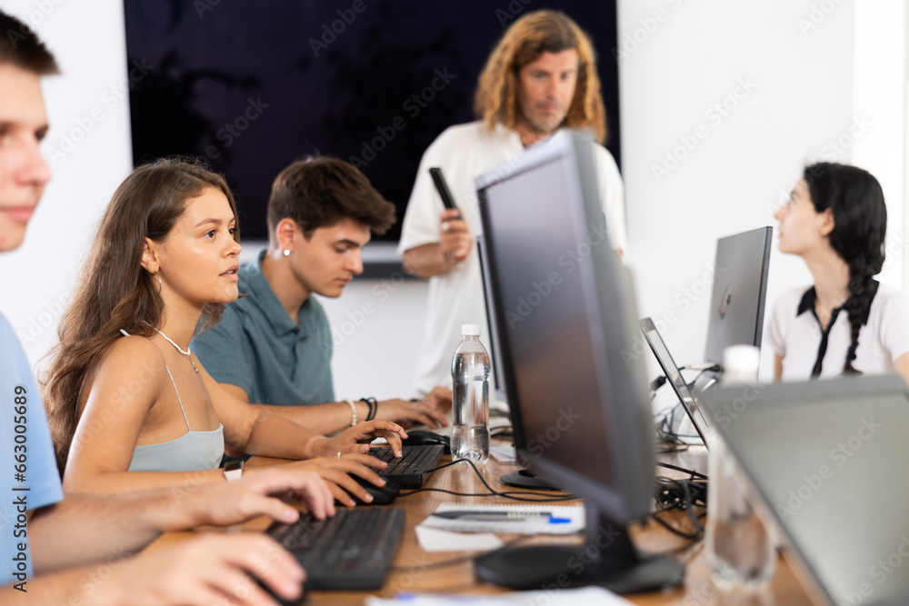 In group of students attending computer courses, female student attentively looks at monitor screen and does performs educational control work