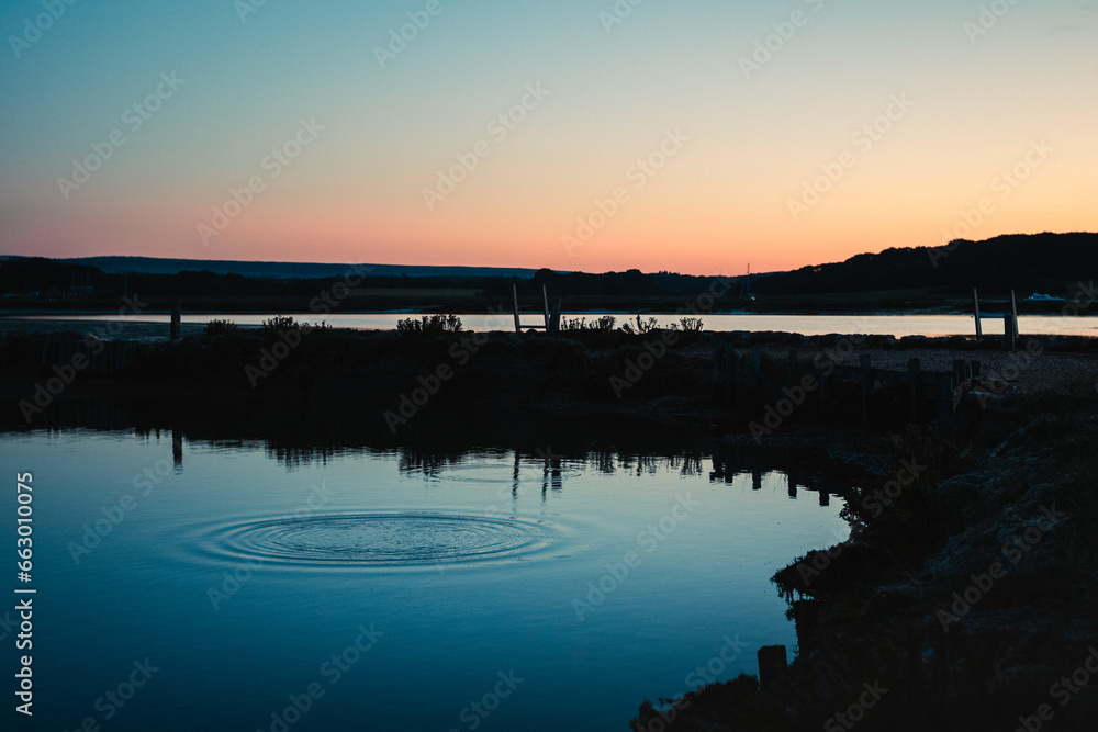 Fototapeta premium A pebble creates a splash of water in a lake at twilight