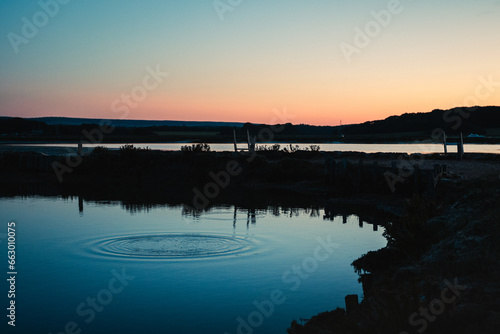 A pebble creates a splash of water in a lake at twilight