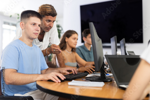 Male teacher of computer courses helps young man student to figure out understand with performance of difficult task  master dark