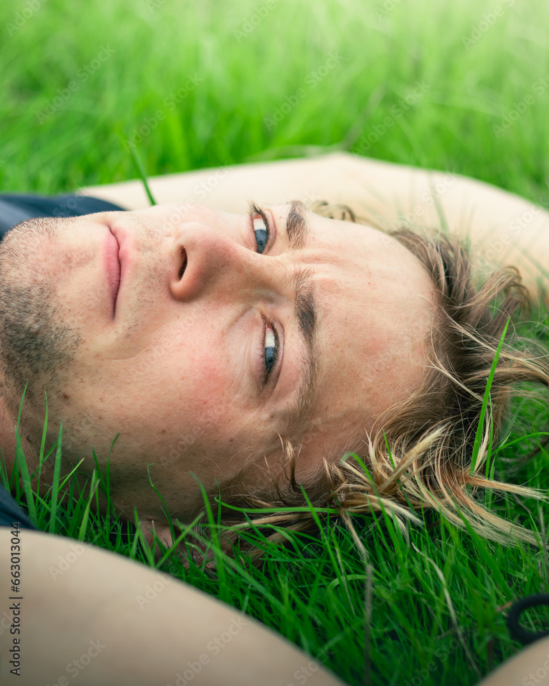 A man looks directly into the camera while lying in a field A man looks directly into the camera while lying in a field