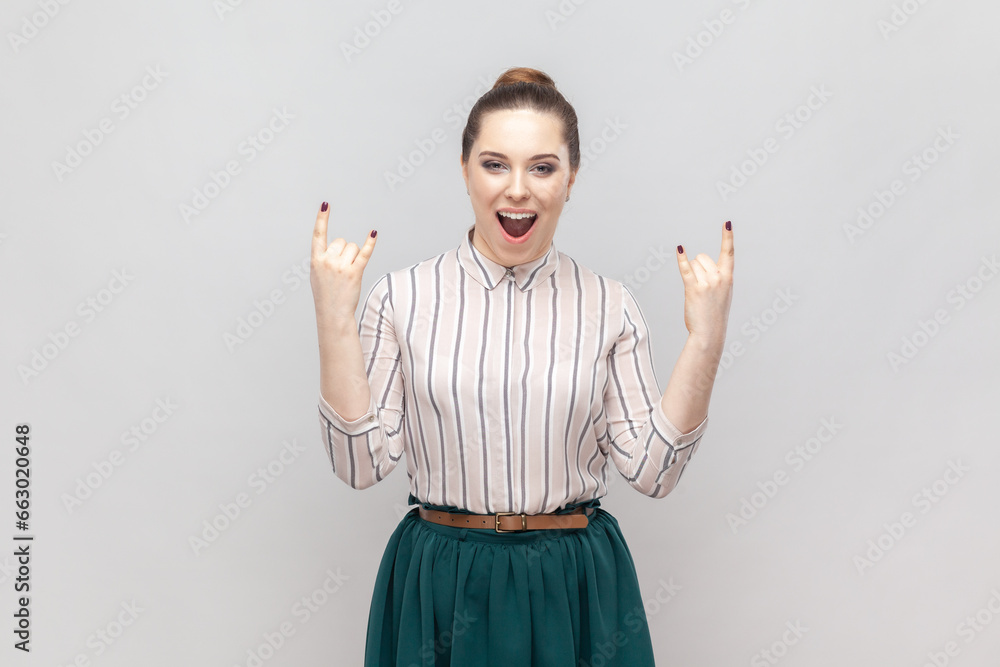 Φωτογραφία Portrait of excited positive happy woman wearing striped shirt and green skirt showing rock and roll gesture, having fun at festival, screaming