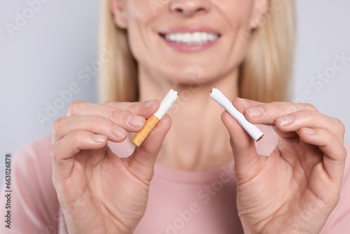 Woman with broken cigarette on light grey background, closeup. Stop smoking concept