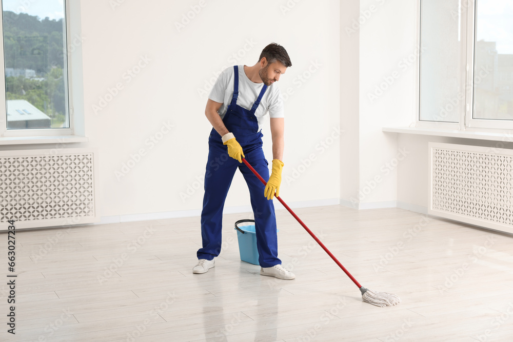 Man in uniform cleaning floor with mop indoors Man in uniform cleaning floor with mop indoors