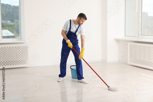 Man in uniform cleaning floor with mop indoors