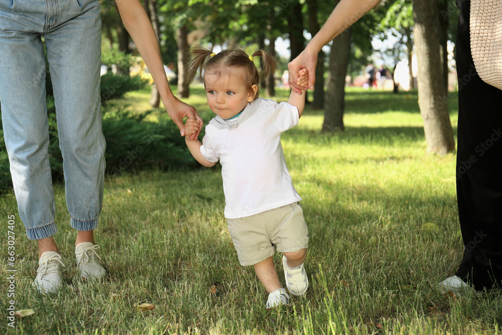 Women supporting baby girl while she learning to walk in park Women supporting baby girl while she learning to walk in park
