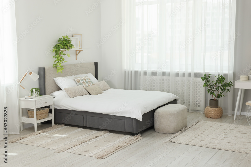 Fototapeta premium Stylish bedroom interior with large comfortable bed, ottoman and bedside table