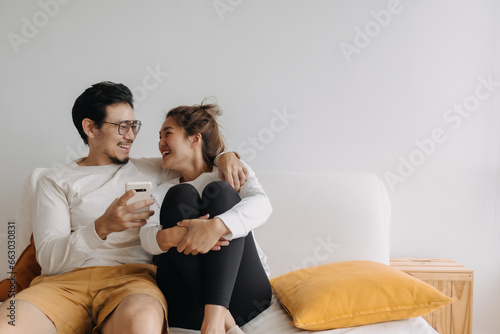 Happy lovely asian couple sharing smartphone to watch together in living room.